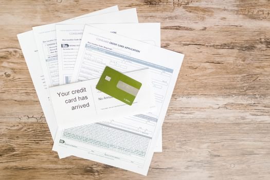 Top view of credit card and application documents on wooden surface.